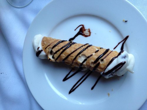 A cannoli filled with cream and drizzled with chocolate sauce, served on a white plate.