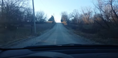 A gravel road leads uphill, flanked by bare trees and a clear blue sky in the background.