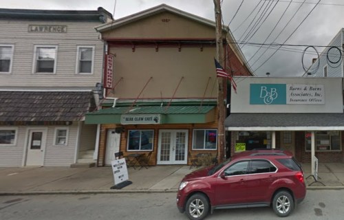 A street view of a small town with a restaurant and a business office, featuring parked cars and utility poles.