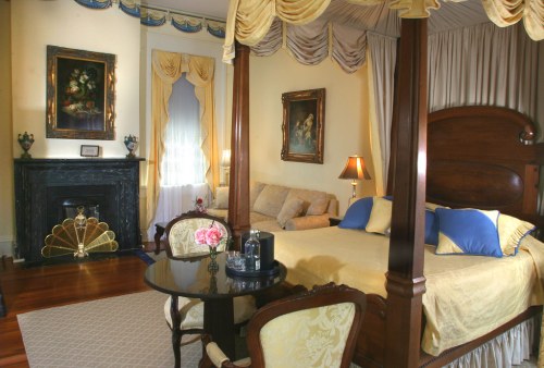 Luxurious bedroom with a four-poster bed, elegant decor, a cozy seating area, and a decorative fireplace.