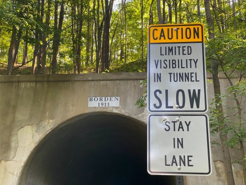 A caution sign near a tunnel entrance warns of limited visibility and advises to slow down and stay in lane.