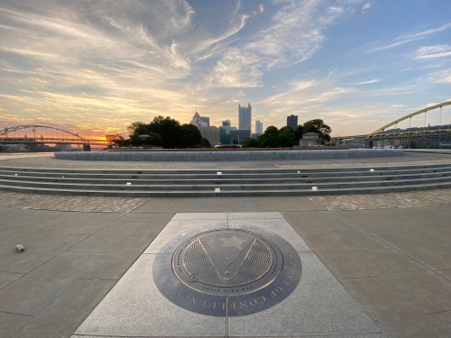 A scenic view of a city skyline at sunset, featuring a circular emblem in the foreground and bridges in the background.
