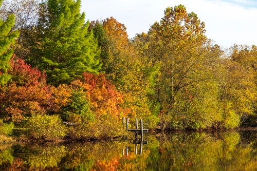 A serene lake surrounded by vibrant autumn foliage and a wooden dock reflecting in the calm water.
