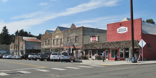 A small town street featuring historic buildings, shops, and parked cars under a clear blue sky.