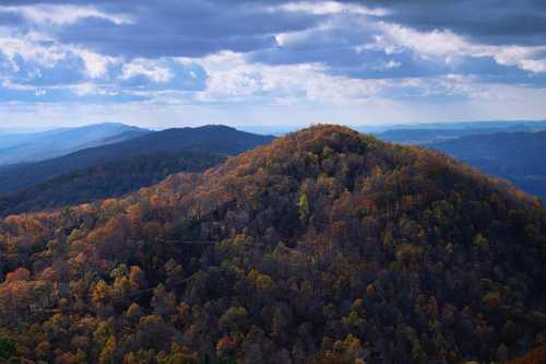 A scenic view of rolling mountains covered in autumn foliage under a cloudy sky.