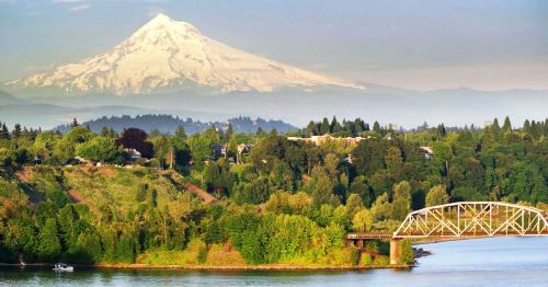 A scenic view of a mountain in the background, lush green hills, and a bridge over a river.