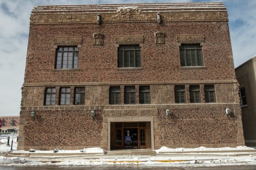 Historic brick building with intricate carvings, large windows, and a snowy foreground under a cloudy sky.