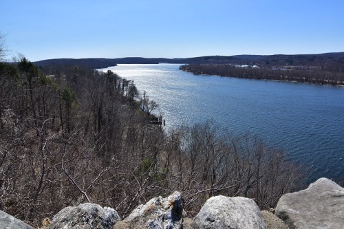 A scenic view of a river winding through a landscape of bare trees and hills under a clear blue sky.