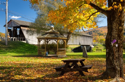 A picturesque scene featuring a gazebo, picnic table, and a covered bridge surrounded by autumn foliage.