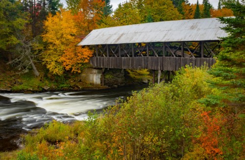 A scenic view of a covered bridge over a river, surrounded by vibrant autumn foliage.