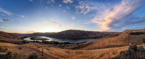 Panoramic view of a river winding through golden hills under a colorful sunset sky.