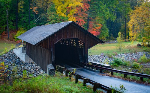 A rustic covered bridge surrounded by vibrant autumn foliage and a winding road leading into the structure.