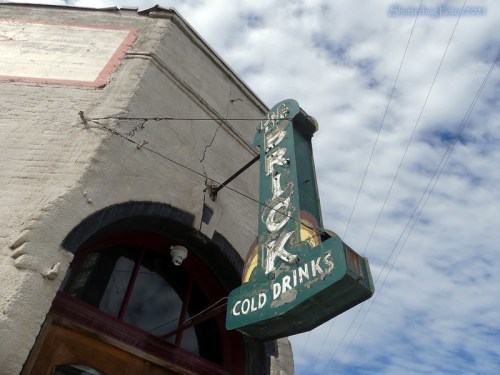 Vintage sign for "Cold Drinks" hanging from a building under a cloudy sky.