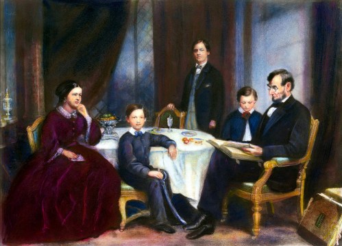 A historical family portrait featuring five individuals seated around a table, with a focus on a man reading.