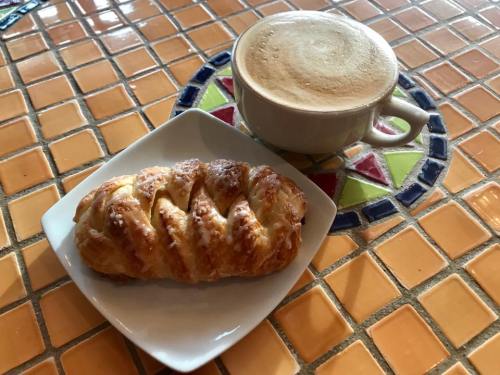 A cup of coffee next to a pastry on a white plate, set on a colorful tiled table.