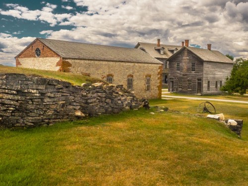 Historic buildings with stone walls and grassy areas under a cloudy sky.