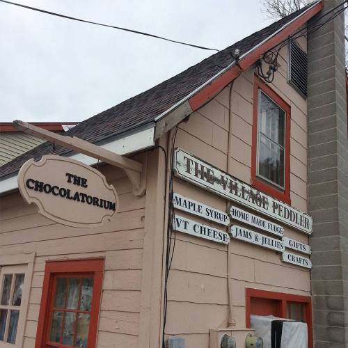 Signage for "The Chocolatorium" and "The Village Peddler," featuring homemade goods and crafts on a quaint building.