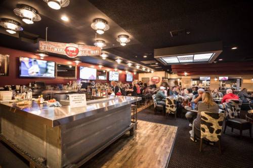 A lively bar scene with patrons seated at tables, a long bar, and multiple TVs displaying sports.