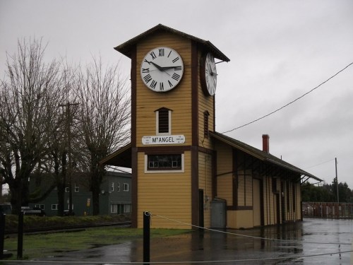 Historic train station with a large clock tower, surrounded by trees and a rainy sky.