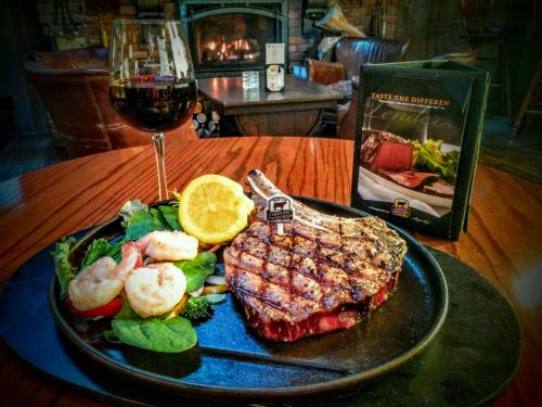 A beautifully plated steak with shrimp, greens, and a lemon slice, accompanied by a glass of red wine and a menu.