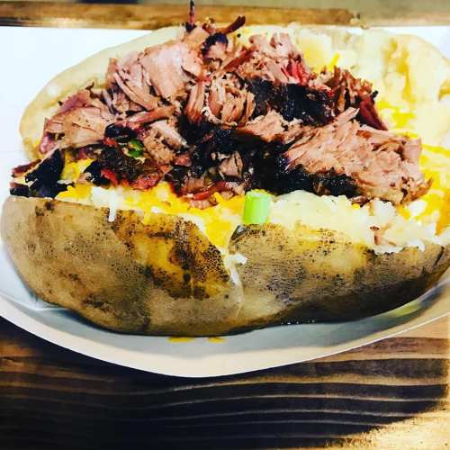 A loaded baked potato topped with shredded meat, cheese, and green onions on a wooden plate.