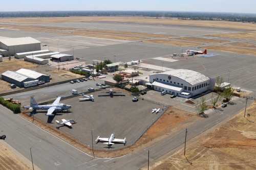 Aerial view of an airport with several planes, hangars, and a runway in a dry, open landscape.