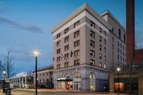 Historic hotel building at dusk, featuring large windows and flags, with streetlights illuminating the scene.