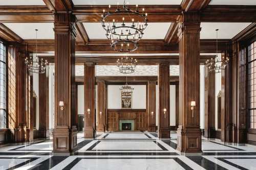 Elegant interior featuring tall wooden columns, chandeliers, and a marble floor in a spacious, well-lit room.