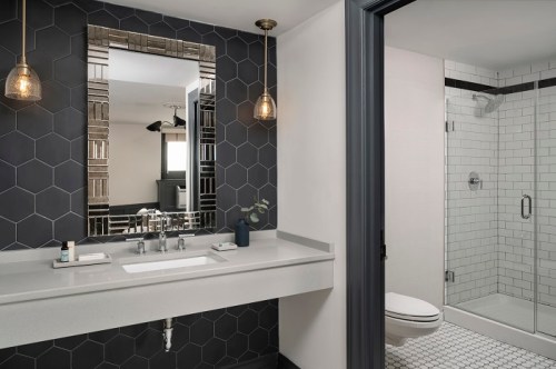 Modern bathroom featuring a hexagonal tile wall, sleek sink, and a glass shower enclosure. Elegant lighting fixtures above.