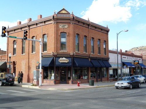 Historic brick building on a corner, featuring large windows and awnings, with cars and pedestrians nearby.