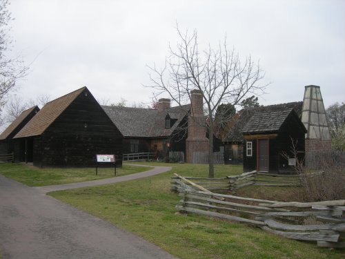 Historic buildings with wooden exteriors and a chimney, set in a grassy area with a path and trees.