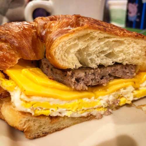 A croissant sandwich filled with layers of scrambled eggs, cheese, and sausage patty.