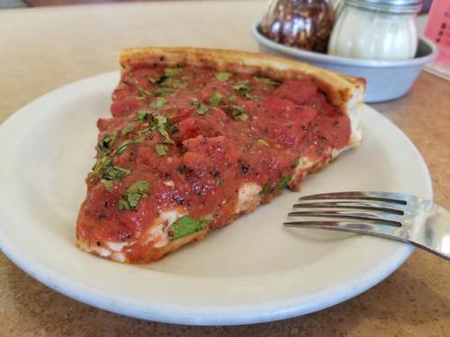 A slice of pizza topped with tomato sauce and fresh herbs on a white plate, with a fork beside it.