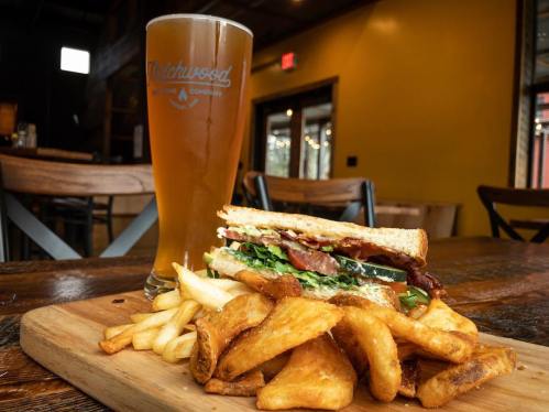 A sandwich with lettuce and bacon, served with golden fries and a pint of beer on a wooden table.