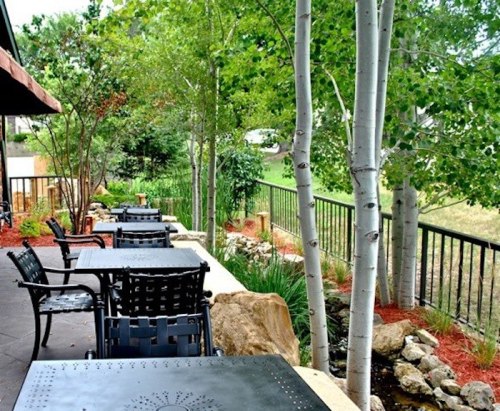 A peaceful outdoor patio with black tables and chairs, surrounded by greenery and trees.