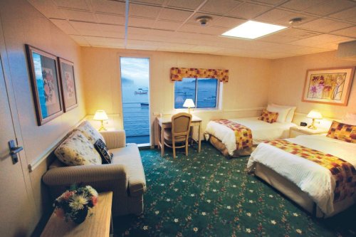 Cozy hotel room with two beds, a sofa, desk, and ocean view through a window. Floral decor and warm lighting.