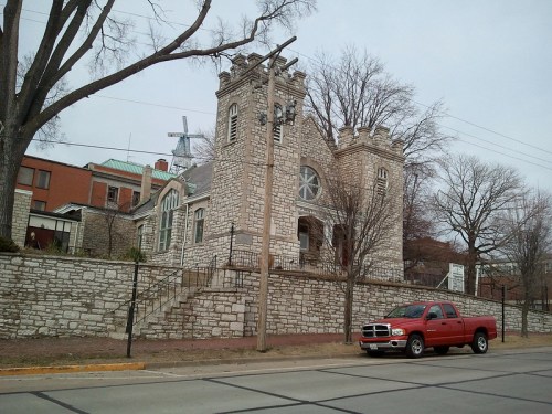 Historic stone building with castle-like features, surrounded by trees and a red truck parked nearby.