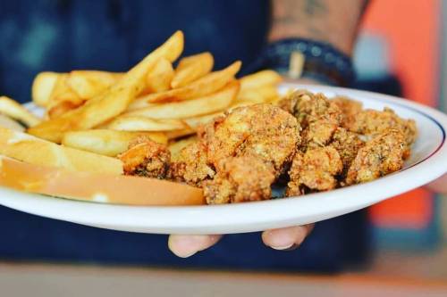 A plate of crispy fried chicken, golden fries, and slices of bread held by a person.