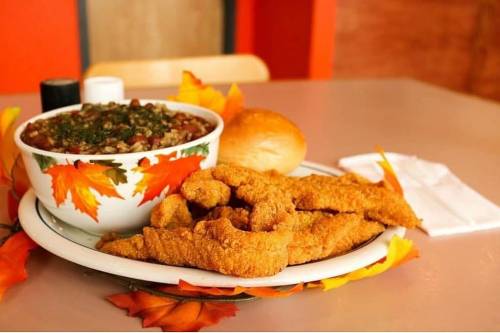 A plate of crispy fried chicken strips, a bowl of chili, a roll, and autumn leaves as decoration on a table.