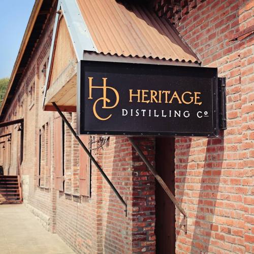 Sign for Heritage Distilling Co. on a brick building with a rustic roof.