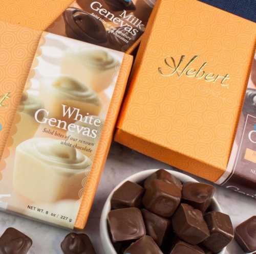 Boxes of Hebert chocolates, including milk and white varieties, with a bowl of chocolate pieces on a marble surface.