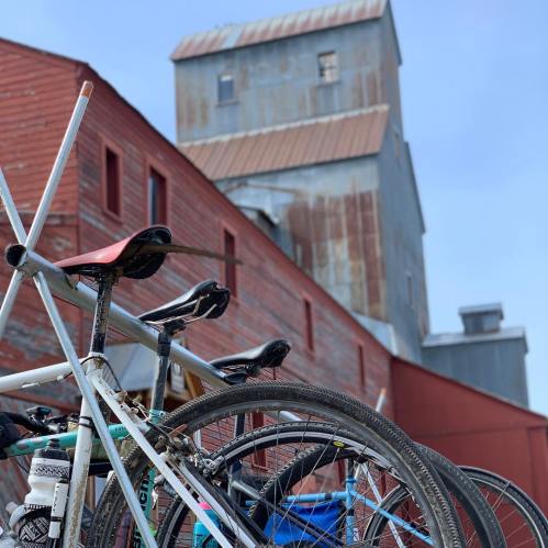 A close-up of bicycles leaning against a red barn with a tall, weathered building in the background.