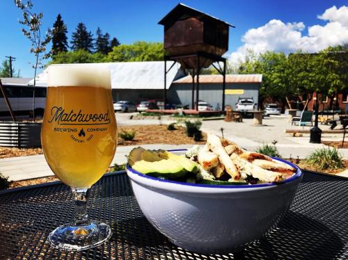 A glass of beer next to a bowl of salad with grilled chicken, set outdoors with a rustic building in the background.