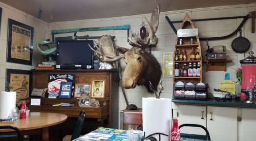 A rustic diner interior featuring a mounted moose head, wooden tables, and various vintage decor items.