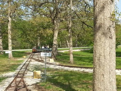 A narrow railway track winds through a green park, with trees and a sign for Coates St. in the foreground.