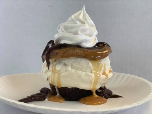 A decadent dessert featuring a cupcake topped with ice cream, whipped cream, and drizzled with chocolate and caramel sauces.
