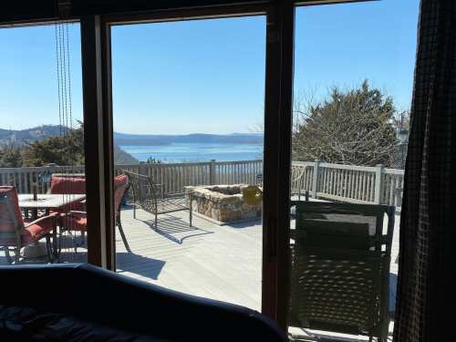 A scenic view of a lake and trees from a large window, with outdoor seating on a deck.