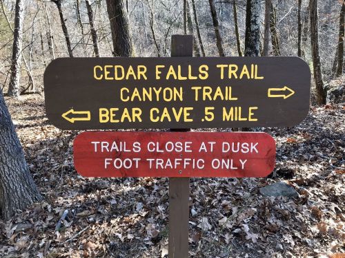 Trail sign indicating Cedar Falls Trail, Canyon Trail, and Bear Cave (0.5 miles), with foot traffic only and dusk closure.