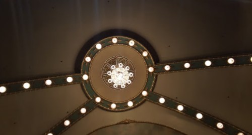 A decorative ceiling with a central chandelier and circular light fixtures along the edges.