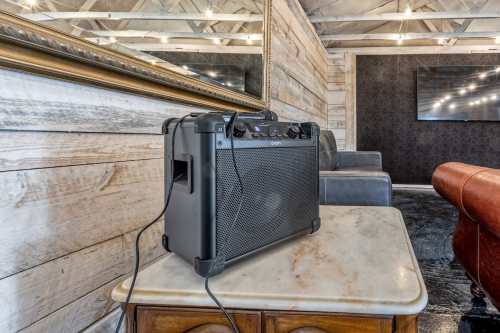 A portable speaker sits on a marble table in a rustic room with wooden walls and cozy seating.